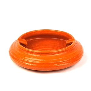 May include: A round, orange ceramic ashtray with a wide, shallow bowl and two built-in rests. The ashtray has a textured, ridged surface and is set against a white background. This item is suitable for home decor.
