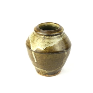 May include: A small, handcrafted ceramic vase with a rounded body and a narrow opening. The vase features a dark brown base with lighter brown and cream-colored accents, creating a rustic, textured appearance. The vase is likely suitable for displaying small flowers or decorative items.