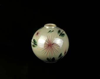 Puede incluir: Un jarrón de cerámica esférico con un acabado de esmalte craquelado en color beige claro. La superficie está decorada con motivos pintados a mano de flores rosadas en forma de estrella y hojas verdes dispuestas alrededor del cuerpo. Tiene una abertura.