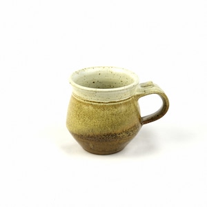 May include: A small, brown and white ceramic mug with a speckled glaze. The mug has a rounded body and a handle.