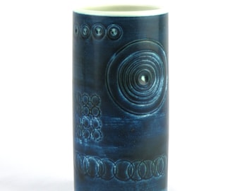 May include: A blue ceramic vase with a geometric pattern of circles and rings. The vase is cylindrical in shape and has a white rim.