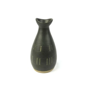 Puede incluir: Una botella de sake de cerámica verde oscuro con una parte superior curva única y un diseño geométrico texturizado. La botella tiene una base de color beige claro y está sobre un fondo blanco. Esta botella decorativa es ideal para servir sake.