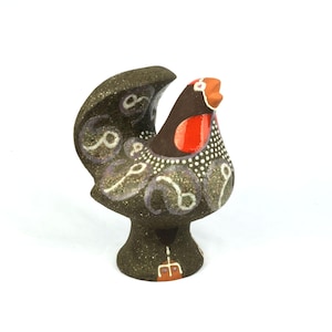 May include: A ceramic rooster figurine with a dark brown body, adorned with white and purple swirls. The rooster has a red breast and a white dotted pattern. The beak is orange, and the figurine stands on a pedestal base.