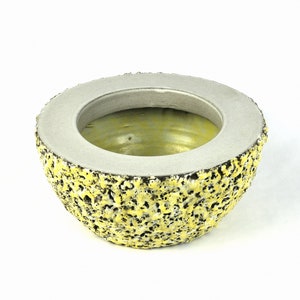 May include: A yellow ceramic planter with a textured exterior and a smooth, grey interior. The planter is shaped like a half sphere.