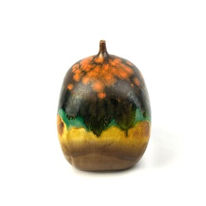 May include: A small, round ceramic vase with a mottled glaze in shades of brown, green, and orange. The vase has a narrow neck and a wide, rounded base.