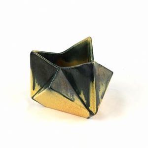 Puede incluir: Un pequeño macetero de cerámica geométrico con un diseño de papel doblado. El macetero está esmaltado en tonos amarillos y verdes.