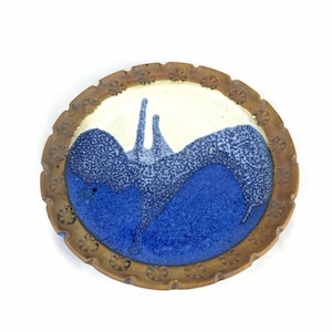 May include: A round ceramic plate with a brown rim and a blue and white glaze. The glaze has a speckled pattern and a wavy design.