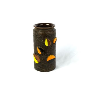 May include: A cylindrical brown vase with a textured surface and a dark brown rim. The vase is decorated with a stylized branch featuring colorful leaves in yellow, orange, and brown. The vase is approximately 18 cm tall.