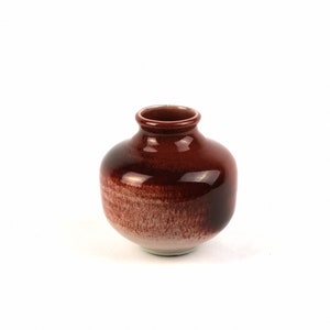 May include: A small, round, brown ceramic vase with a white glaze on the bottom.