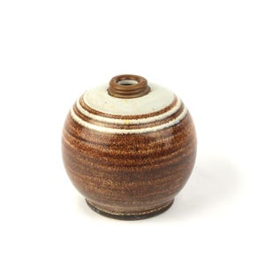 May include: A small, round ceramic vase with a brown and white striped pattern. The vase has a narrow opening at the top and a dark brown base. The overall design is simple and elegant, suitable for home decor.