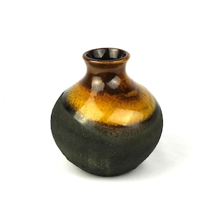 May include: A small, round ceramic vase with a narrow neck and a wide, bulbous body. The lower portion of the vase features a matte, textured black finish, while the upper section and rim are glazed in a smooth, glossy gradient of amber and brown.