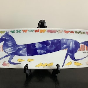 Op de afbeelding: Rechthoekige witte keramische serveerschaal met een blauwe paardenillustratie. De schaal heeft een rand van kleurrijke vlinders en kleine gele vogels. Gesigneerd "Andy Warhol".