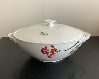 Peut inclure: Une soupière en céramique blanche avec couvercle assorti, ornée d'une petite illustration de papillon sur le dessus et d'un motif botanique détaillé de baies rouges et de feuilles vertes sur le côté, avec deux anses et un bouton central.