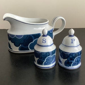 Op de afbeelding: Een witte keramische juskom met een blauw-wit wolkenpatroon en een bijpassend setje zout- en peperstrooiers. De strooiers zijn gemarkeerd met "S" en "P".