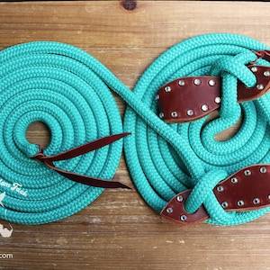 Op de afbeelding: Een turquoise touwhalster met bruine lederen accenten en strass. Het halster is opgerold en klaar voor gebruik. "Rachel Fail Custom Tack" en "www.rfftack.com" zijn op het touw gedrukt.