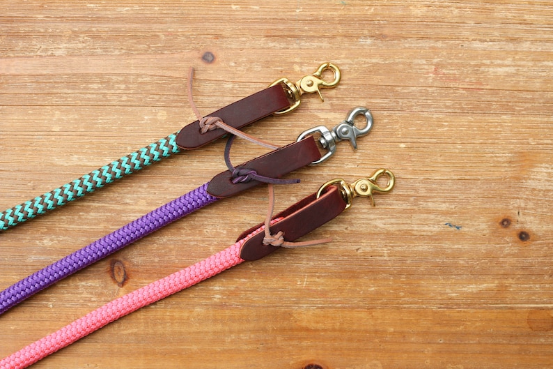 May include: Three leather dog leashes with different colored ropes. The leashes are brown leather with a brass hook on the end. The ropes are teal and brown, purple, and pink.