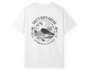 Könnte beinhalten: Weißes T-Shirt mit einem kreisförmigen Aufdruck, der eine Möwe mit Hut und Surfbrett zeigt. Der Aufdruck enthält den Text "Salty Days Ahead" und "Saltwater Co. Scituate". Das Design ist in Grau- und Blautönen gehalten.