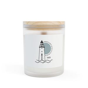 May include: A white candle in a glass jar with a wooden lid. The label features a black and white illustration of a lighthouse with the text "MINOTS LIGHT" and coordinates. The number "143" is below the lighthouse.