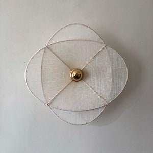 May include: A white, circular, layered, fabric wall sconce with a gold sphere in the centre.