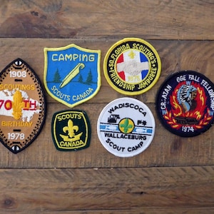May include: A selection of vintage Boy Scout patches with diverse designs and text. Patches include "Camping Scouts Canada", "So. Florida Scouting Jamboree", and "70th Birthday 1978". The patches are displayed on a wooden surface.