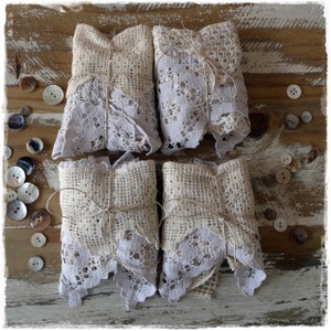 May include: Four white lace-wrapped packages tied with twine, arranged on a rustic wooden surface. The packages are made of delicate white lace and have a vintage, rustic aesthetic.