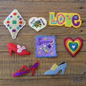 May include: An assortment of colourful embroidered iron-on patches, including a heart with rainbow stripes, a purple patch with a scorpion, a red and white shoe, a blue shoe, a heart with a sunflower, a square patch with a geometric design, and a yellow patch with the word "LOVE" in colourful letters.