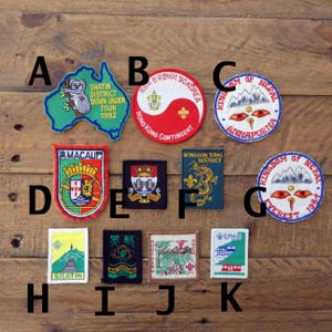 Peut inclure: Une collection d'écussons brodés avec divers motifs et textes. Les écussons présentent des images d'un koala, de montagnes, de dragons et de drapeaux. Le texte comprend "SHATIN DISTRICT DOWN UNDER TOUR 1992", "KOWLOON TONG DISTRICT", et "KINGDOM OF NEPAL".