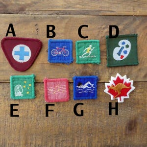 May include: A selection of vintage fabric patches. Designs include a red triangle with a white cross, a blue square with a bicycle, a green square with a runner, and a green square with a painter's palette.