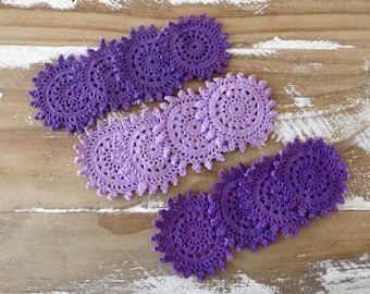 May include: A set of seven crocheted doilies in shades of purple, arranged in a gradient from light to dark. The doilies are made with a delicate, lacy pattern and are perfect for adding a touch of elegance to any home.