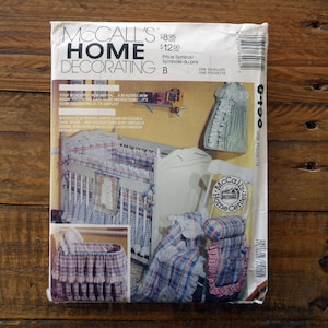 May include: A McCall's Home Decorating sewing pattern envelope, number 6490, featuring illustrations of a plaid crib bedding set, a bassinet with ruffled trim, and a rocking chair cushion set. The white paper envelope includes text and a barcode.