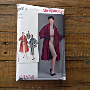 May include: A Simplicity sewing pattern envelope, number 8509, for 1950s vintage style clothing. The package displays illustrations of a long coat, a shorter jacket, and a dress, with sizing information for European sizes 40-48 printed on the front.