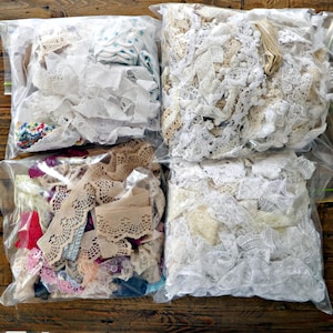 May include: Four clear plastic bags filled with assorted lace and fabric trims. The collection includes white, cream, beige, and tan lace strips, along with small sections of floral, red, pink, and blue patterned fabric scraps and decorative ribbons.