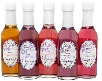 Puede incluir: Cinco pequeñas botellas de vidrio de jarabe aromatizado con etiquetas blancas. Las etiquetas tienen un diseño morado y blanco y dicen "The Sweetest Thing" y "Pure Lavender Syrup". Los sabores son LOL, Lavanda, Pera de lavanda, Vainilla de lavanda y Rosa habanero de lavanda.