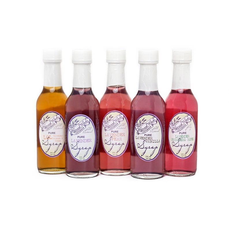May include: Five small glass bottles of flavored syrup with white labels. The labels have a purple and white design and say "The Sweetest Thing" and "Pure Lavender Syrup". The flavors are LOL, Lavender, Lavender Pear, Lavender Vanilla, and Lavender Habanero Rose.