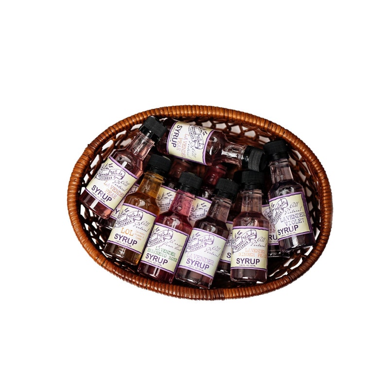 May include: A wicker basket filled with small glass bottles of flavored syrup. The bottles have labels with different flavors, including lavender, pear, ginger, and violet.
