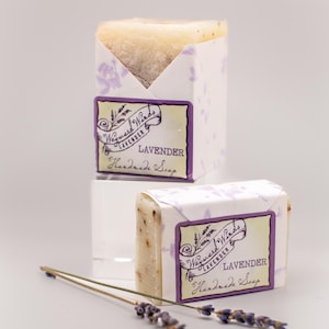May include: Two bars of lavender-scented handmade soap wrapped in white paper with a purple and yellow label that reads "Wayward Winds Lavender Handmade Soap".