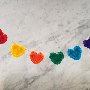Peut inclure: Une guirlande de cœurs en crochet de couleur arc-en-ciel avec des cœurs rouges, orange, jaunes, verts, bleus et violets.