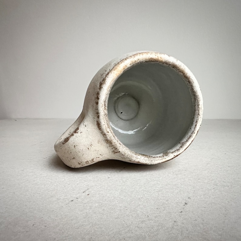 May include: A white ceramic mug with a brown rim and a handle. The mug is empty and the inside is white.