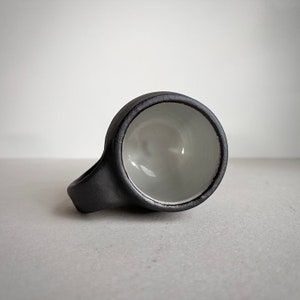 May include: A black ceramic mug with a white interior. The mug has a rounded handle and a wide, shallow bowl.