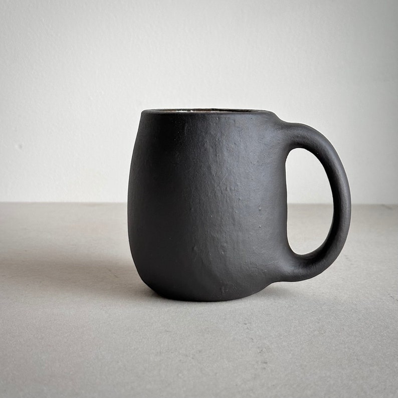 May include: A black ceramic mug with a rounded body and a slightly curved handle.