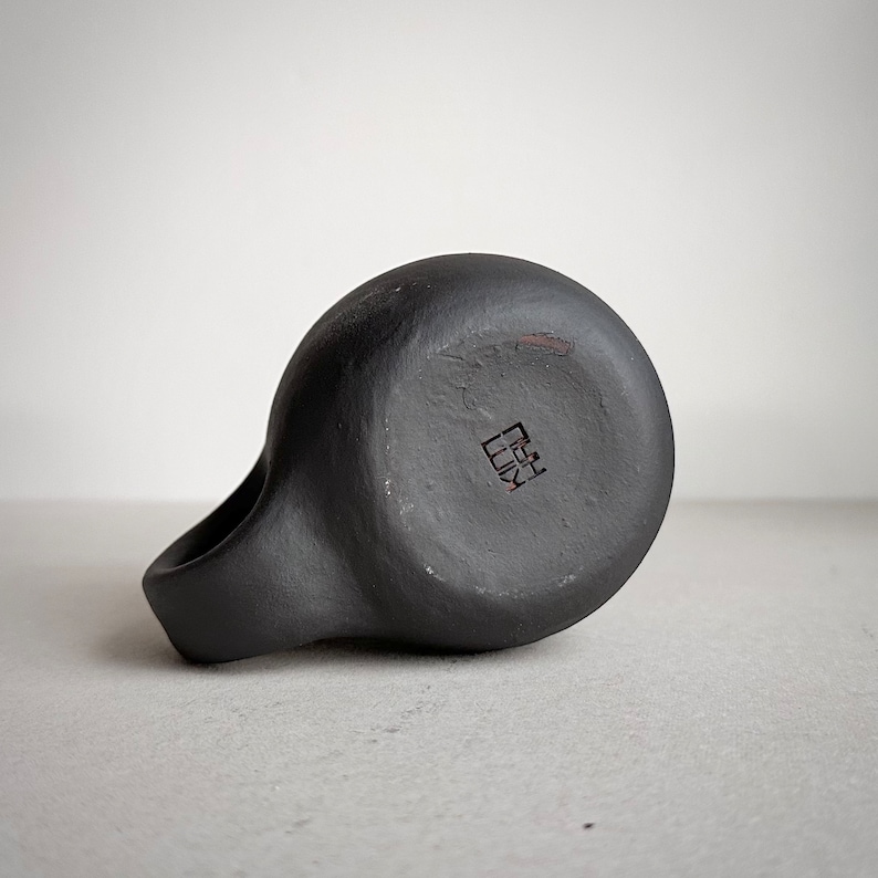 May include: Black ceramic mug with a handle and a square mark on the bottom that reads "陶芸".