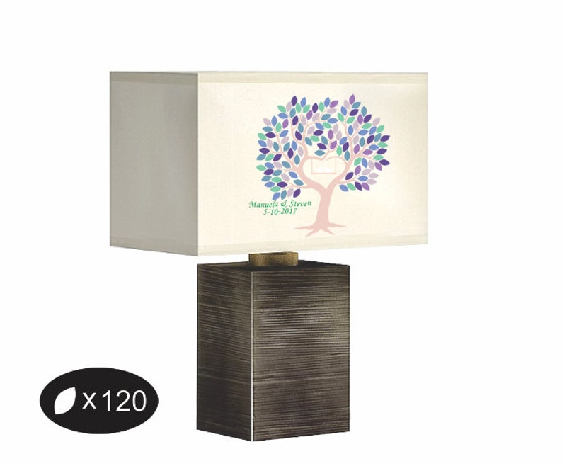 May include: A rectangular lamp with a dark brown base and a cream-colored lampshade. The lampshade features a tree design with purple, blue, and green leaves, a heart-shaped cutout, and the text "Manuela & Steven 5-10-2017".