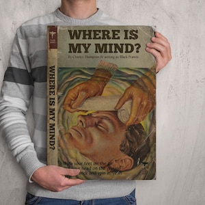 May include: A vintage book cover with a yellowed background and a dark brown title: "Where Is My Mind?" by Charles Thompson IV writing as Black Francis. The cover features a surreal illustration of a person's head being held by two hands, with a bandage on the forehead. The text below the illustration reads: "With your feet on the air and your head on the ground, crick and spin it, yeah."