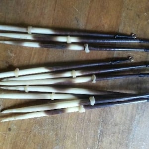 May include: A set of eight brown and white bone knitting needles with black thread and metal rings at the ends.