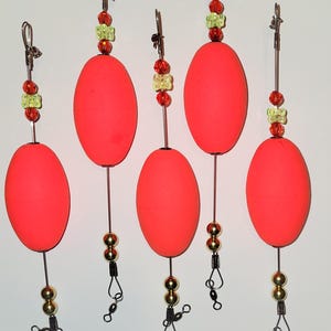 May include: Five bright red fishing bobbers with gold beads and a swivel. Each bobber has a silver wire with a clip at the top and a green and red bead accent.