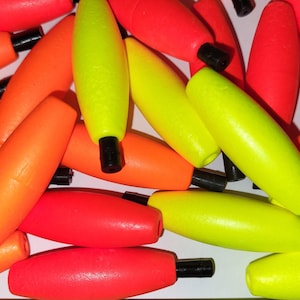 May include: A close-up of a pile of bright orange and yellow bobbers. The bobbers are made of foam and have a black tip.