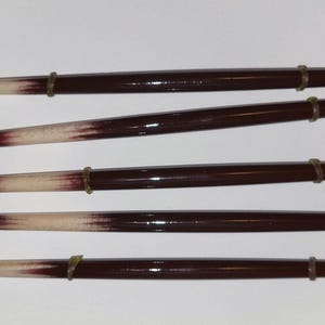 May include: Five wooden dowels with white tips and brown paint. Each dowel has a gold metal ring.