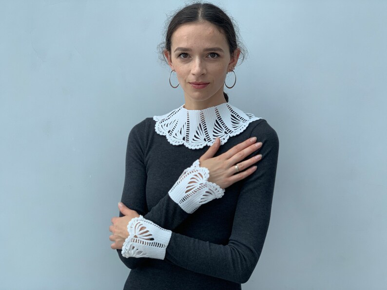 May include: A woman wearing a gray long-sleeved shirt with a white crocheted collar and matching cuffs. The collar and cuffs have a delicate, intricate design.