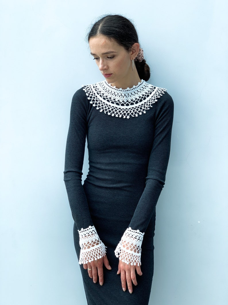 May include: A black long-sleeved dress with a white crocheted collar and cuffs.
