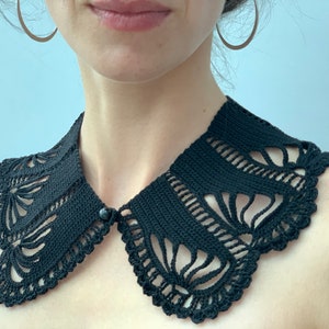 May include: A black crocheted collar with a delicate floral pattern. The collar is made with a fine yarn and has a button closure.